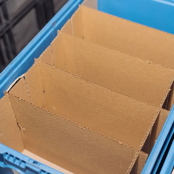 Cardboard divider insert placed inside a blue plastic returnable tote to create multiple compartments.