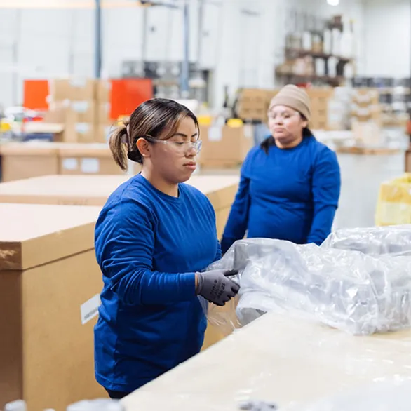 Worker handling an automotive valve cover while adjusting protective plastic around parts staged for inspection.