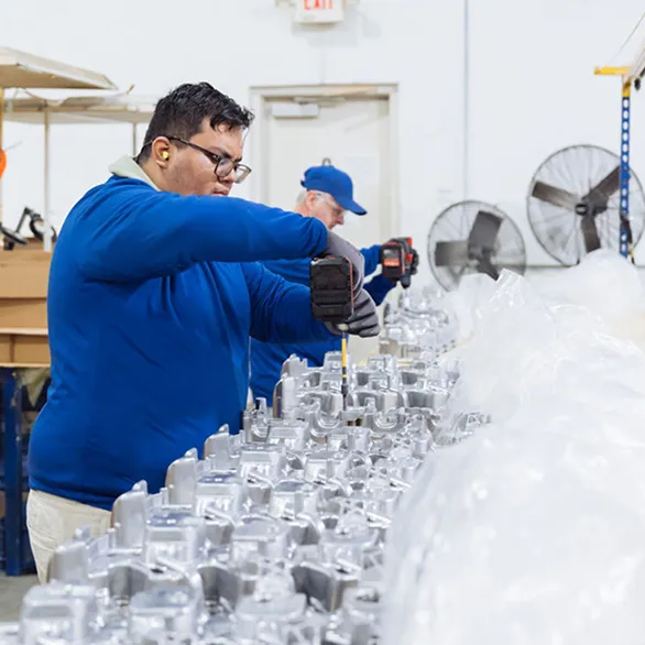 Worker using a cordless drill to rework threaded holes on an automotive valve cover positioned on an inspection table.