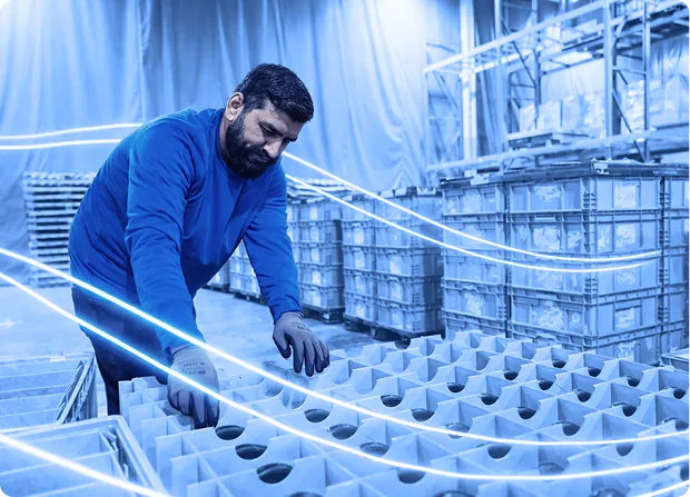 Worker sorting plastic containers inside a warehouse facility with stacked returnable packaging in the background.