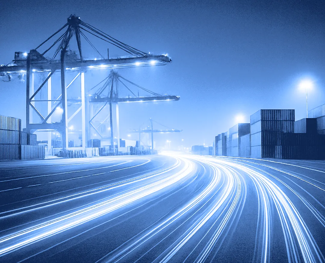 Shipping dock with container cranes and illuminated traffic lanes at night.