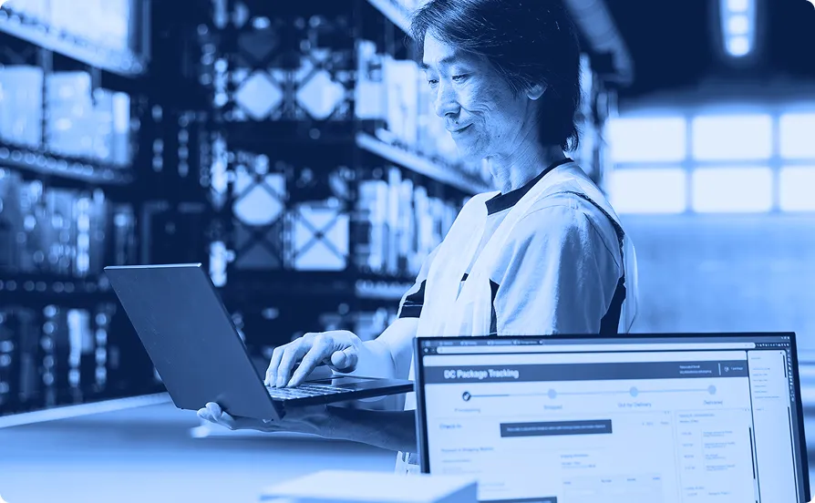 Employee working at a computer workstation inside a warehouse environment.
