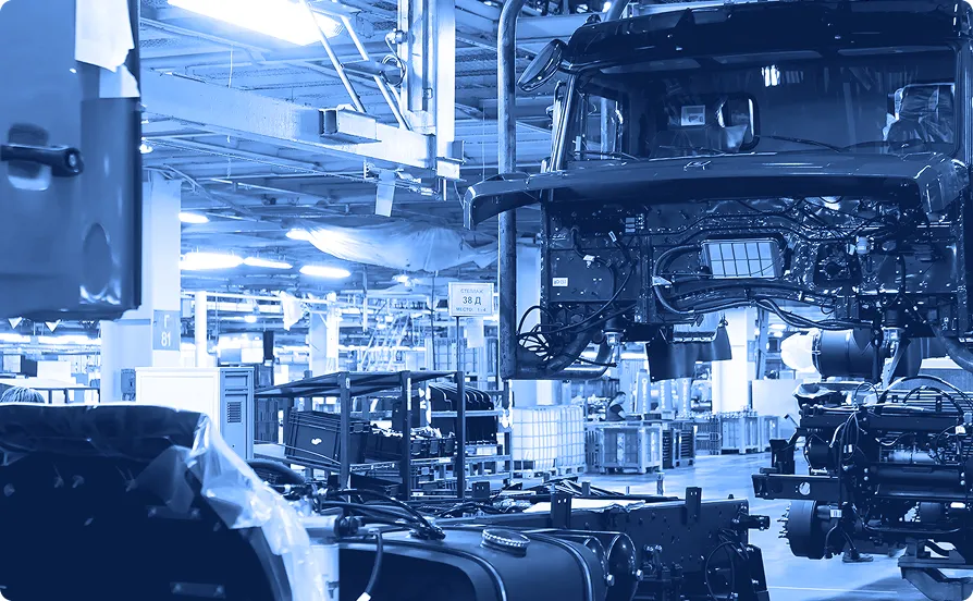 Automobile frames moving through an assembly line surrounded by robotic arms inside a manufacturing facility.
