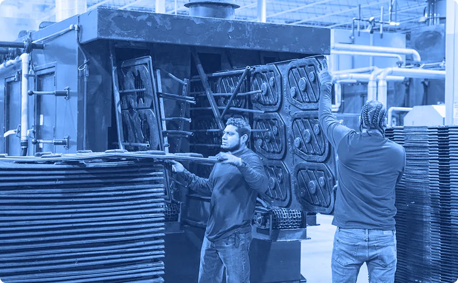 Two workers handling stacked plastic pallets beside a large industrial washing machine inside a warehouse facility.

