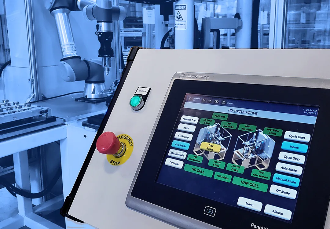Automated robotic assembly cell with collaborative robot, fixture plate, and touchscreen control panel in a manufacturing facility.

