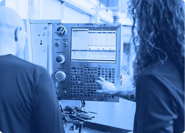 Two operators reviewing data and controls on an industrial machine interface during production.  
