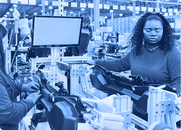 Two technicians assembling components at a fixture-based workstation in a manufacturing facility.