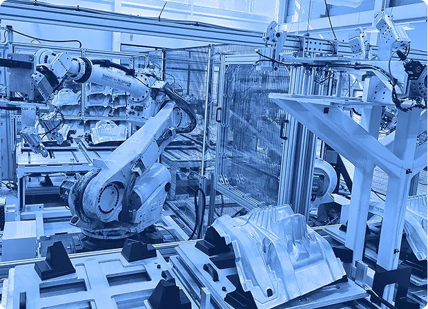 Robotic arms positioned over metal fixtures and molded parts inside a fenced automation cell on a factory floor.