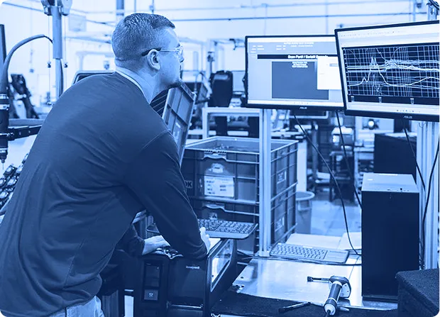 Assembly technician reviewing test data on computer monitors during automated subassembly testing.