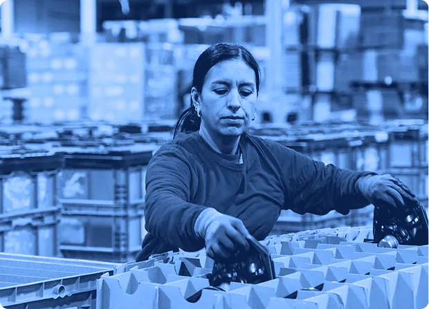 Worker placing components into cardboard inserts on a pallet inside a warehouse packaging area.