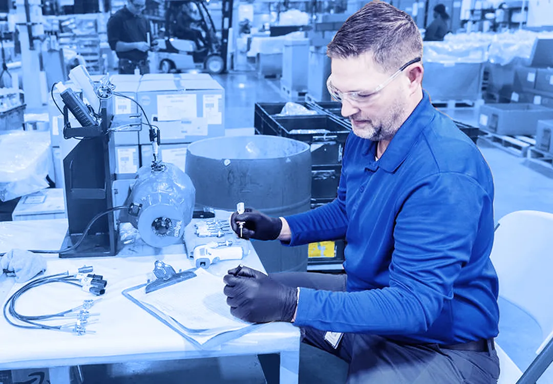Technician inspecting and testing a mechanical component at a workbench in a manufacturing facility.