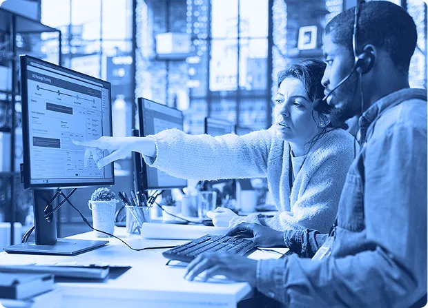 Two employees seated at desks reviewing information on a computer monitor inside an office workspace.     