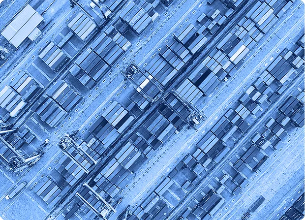 Aerial view of stacked shipping containers arranged in rows at a port or freight yard.  