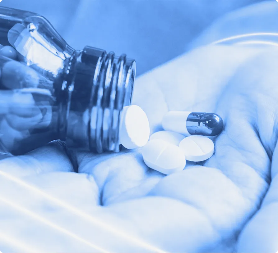 Hand holding prescription pills poured from a bottle against a blurred background.