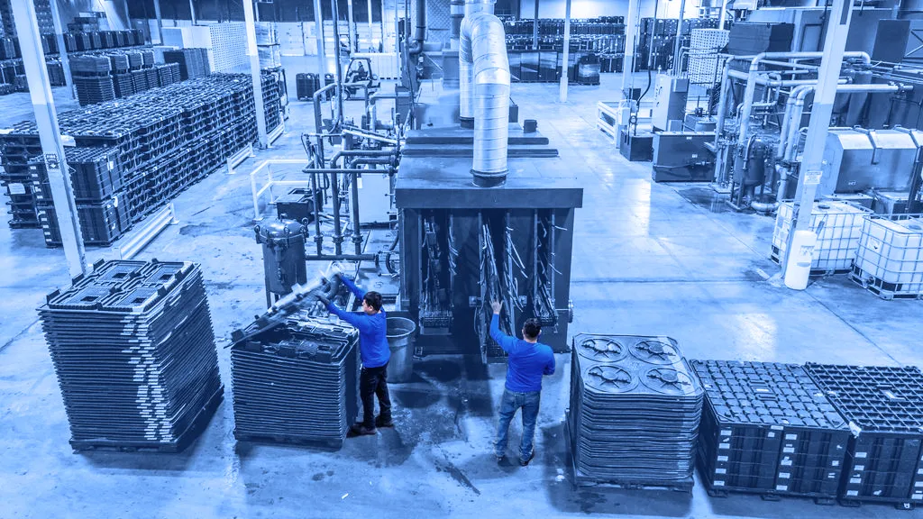 Workers putting staged containers through a high-pressure washing system.
