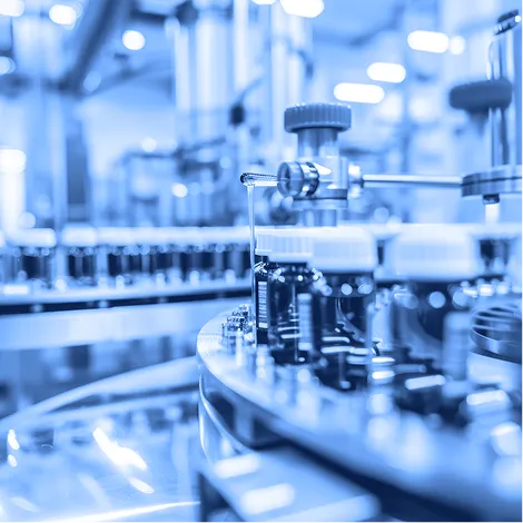 Pharmaceutical technician wearing protective clothing and holding a tablet inside a processing facility.