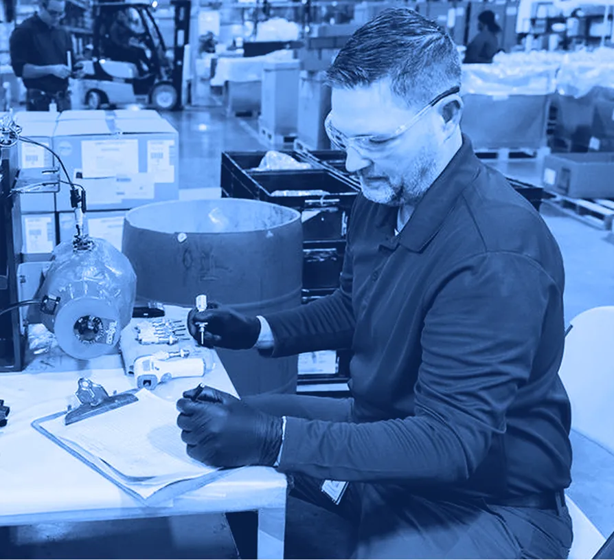 Technician inspecting and testing a mechanical component at a workbench in a manufacturing facility.
