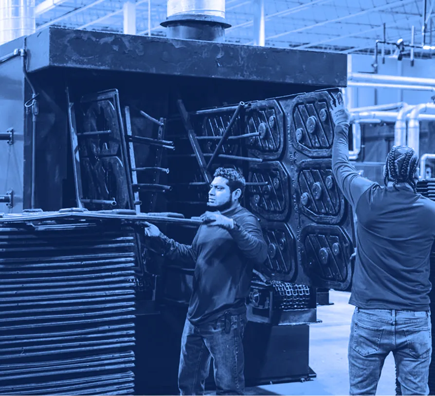 Two workers handling stacked plastic pallets beside a large industrial washing machine inside a warehouse facility.