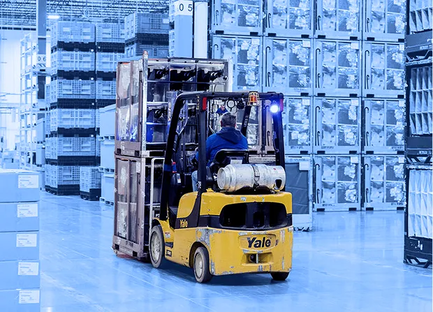 Forklift operator transporting stacked containers through a warehouse supporting assembly operations.