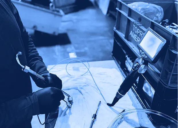 Technician inspecting a mechanical part using a borescope and measurement tools at a workbench. 