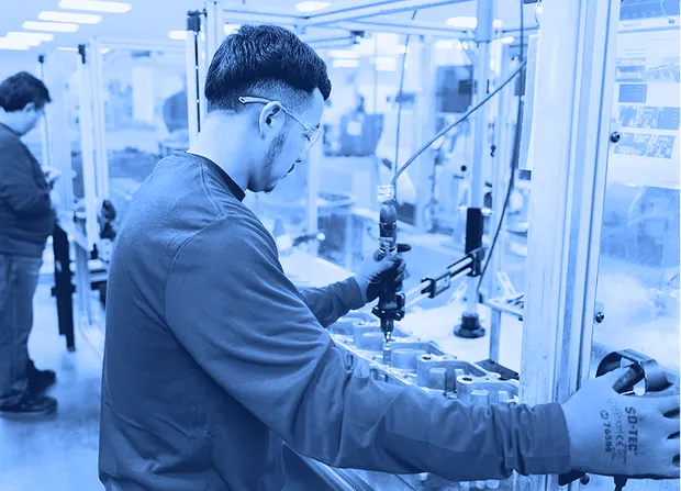 Assembly worker operating a powered tool inside a guarded workstation following safety procedures.