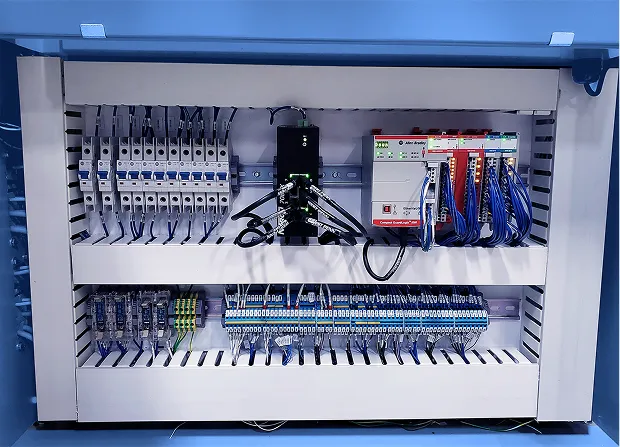 Open electrical control cabinet showing circuit breakers, terminal blocks, programmable controller modules, and organized wiring mounted on DIN rails.