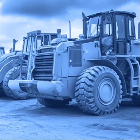 Row of large yellow wheel loaders with front buckets parked on a dirt surface under an overcast sky. 