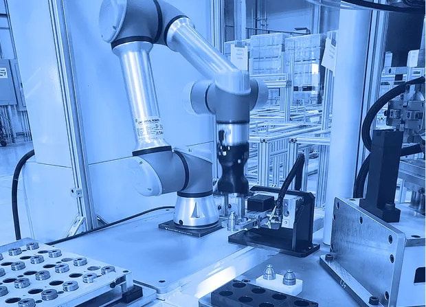 Collaborative robotic arm operating over a worktable with metal fixtures, sensors, and parts inside an enclosed automation cell.  