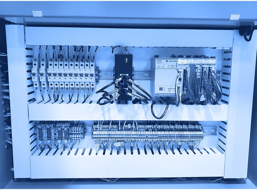 Open electrical control cabinet showing circuit breakers, terminal blocks, programmable controller modules, and organized wiring mounted on DIN rails.