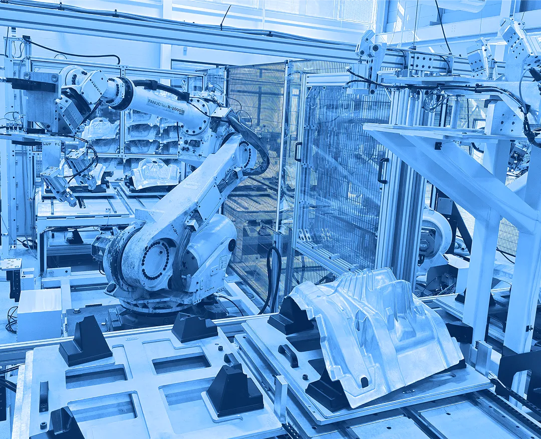 Robotic arms positioned over metal fixtures and molded parts inside a fenced automation cell on a factory floor.