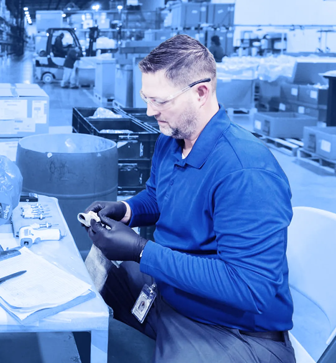 Technician inspecting and testing a mechanical component at a workbench in a manufacturing facility.