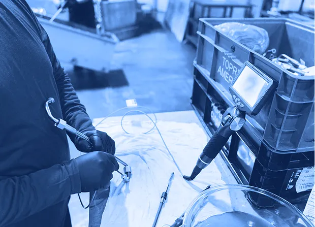 Technician inspecting a mechanical part using a borescope and measurement tools at a workbench.