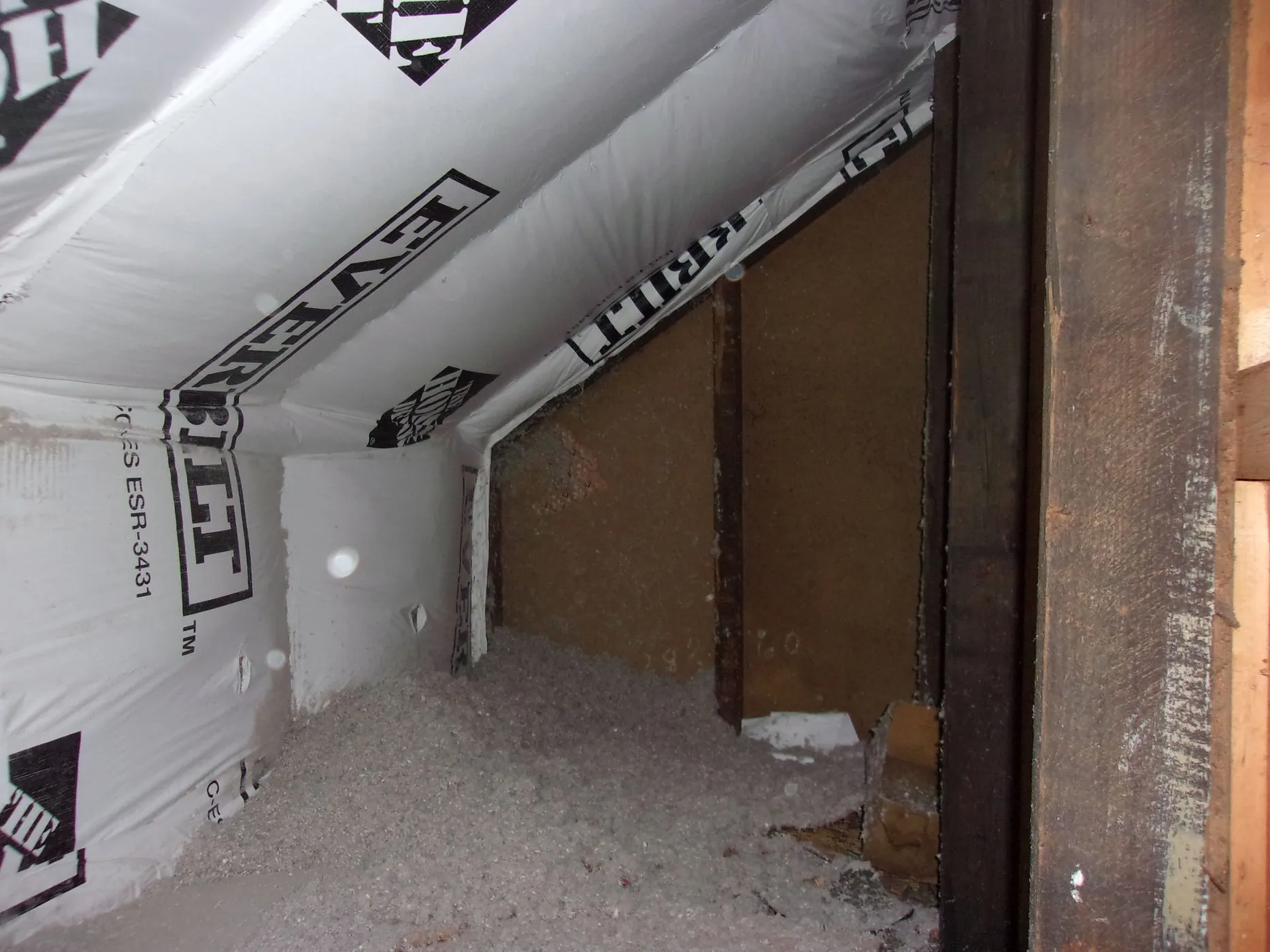 Attic eaves insulated with dense-pack cellulose insulation and covered with protective sheets labeled 'LEVERIT'.