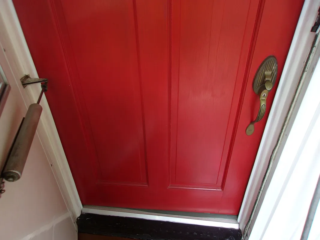 Red front door with antique brass handle and door closer installed on the white door frame.