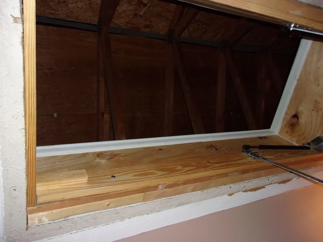 Open attic access framed with wood and showing roof rafters inside.