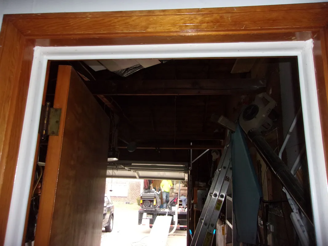 View through a doorway into a dimly lit garage with a partially open garage door and a ladder leaning against the wall.