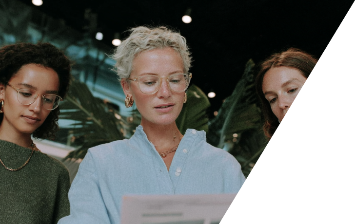 Trois femmes regardant attentivement un document sous une lumière tamisée avec des plantes en arrière-plan.