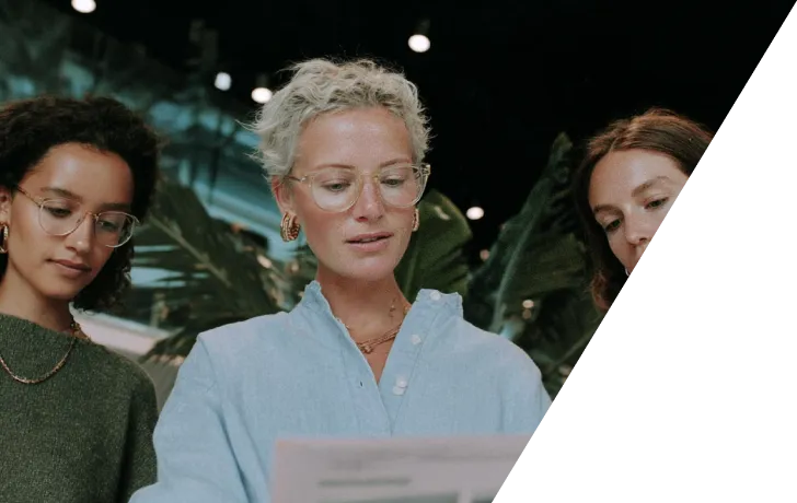 Trois femmes regardant attentivement un document sous une lumière tamisée avec des plantes en arrière-plan.