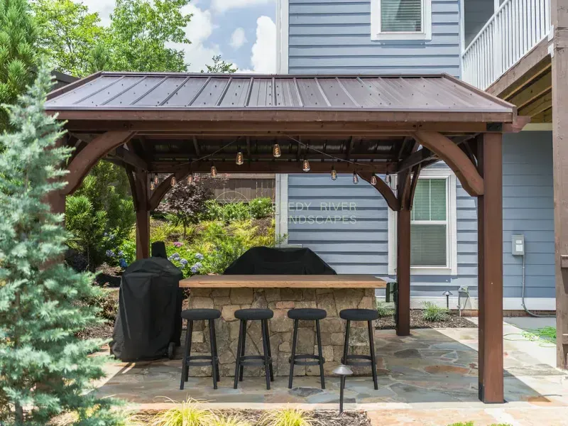 String lights under a pergola with an outdoor kitchen.
