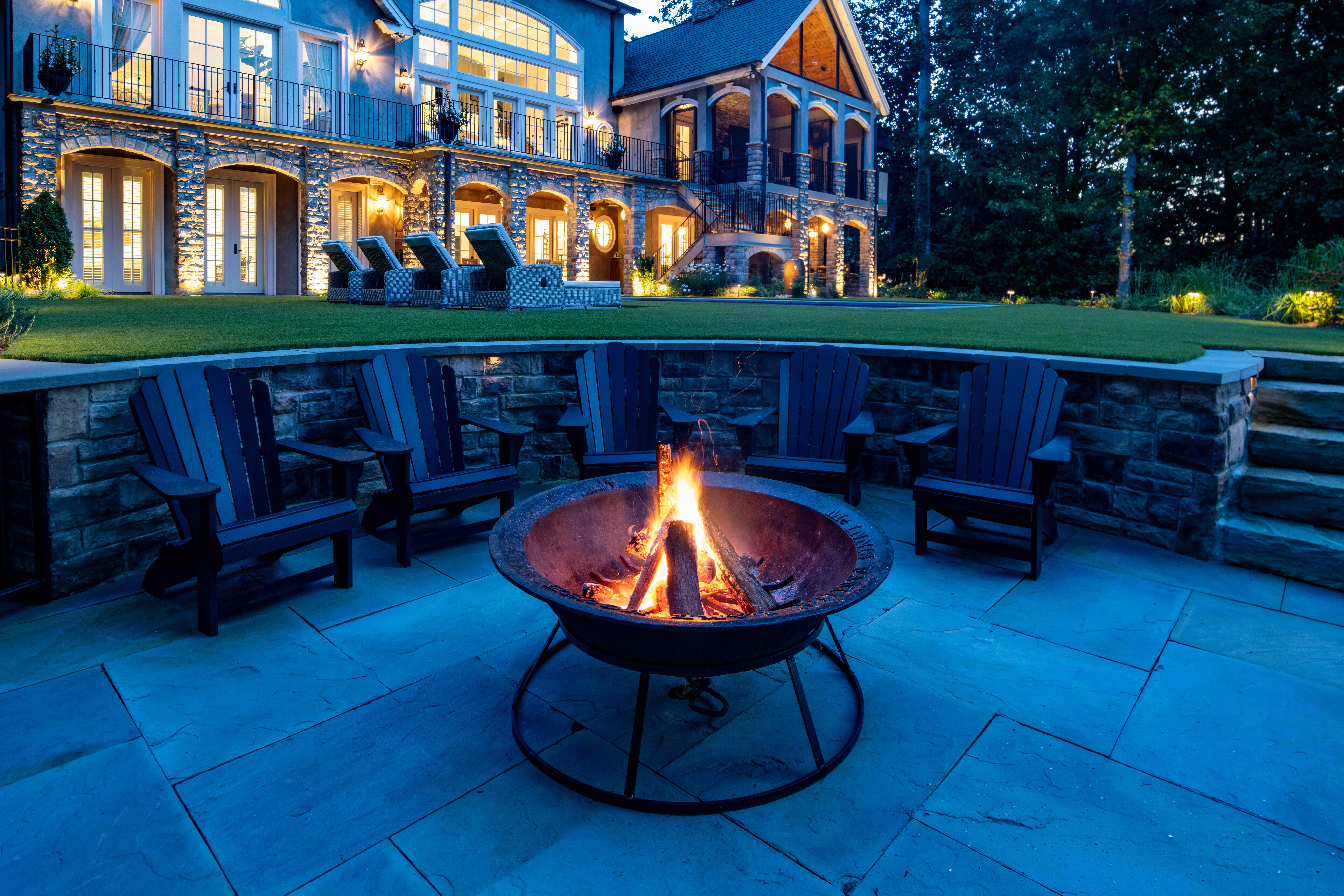 Elegant backyard landscape with custom low voltage lighting illuminating pathways, trees, and patio areas at dusk