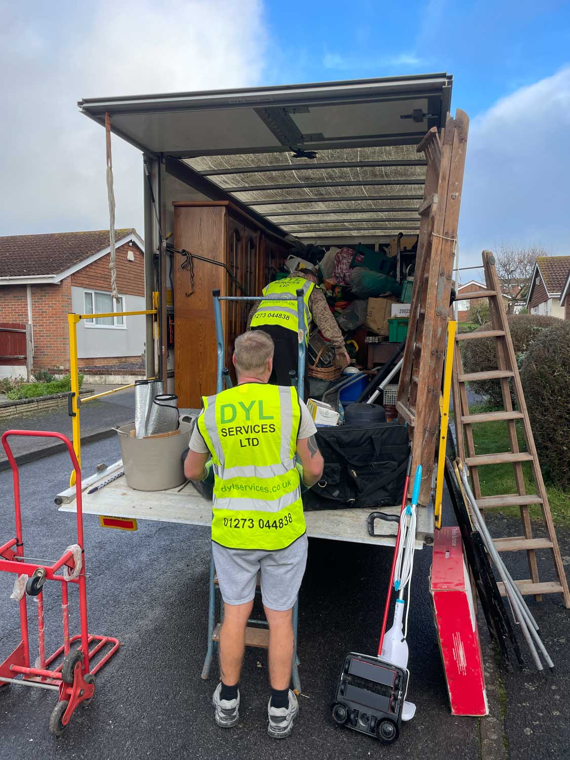 Two DYL workers loading furniture and items into a truck on a residential street.