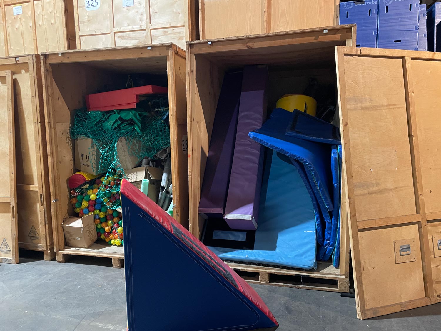 Large wooden crates filled with colorful foam blocks, mats, and play balls in a storage area.