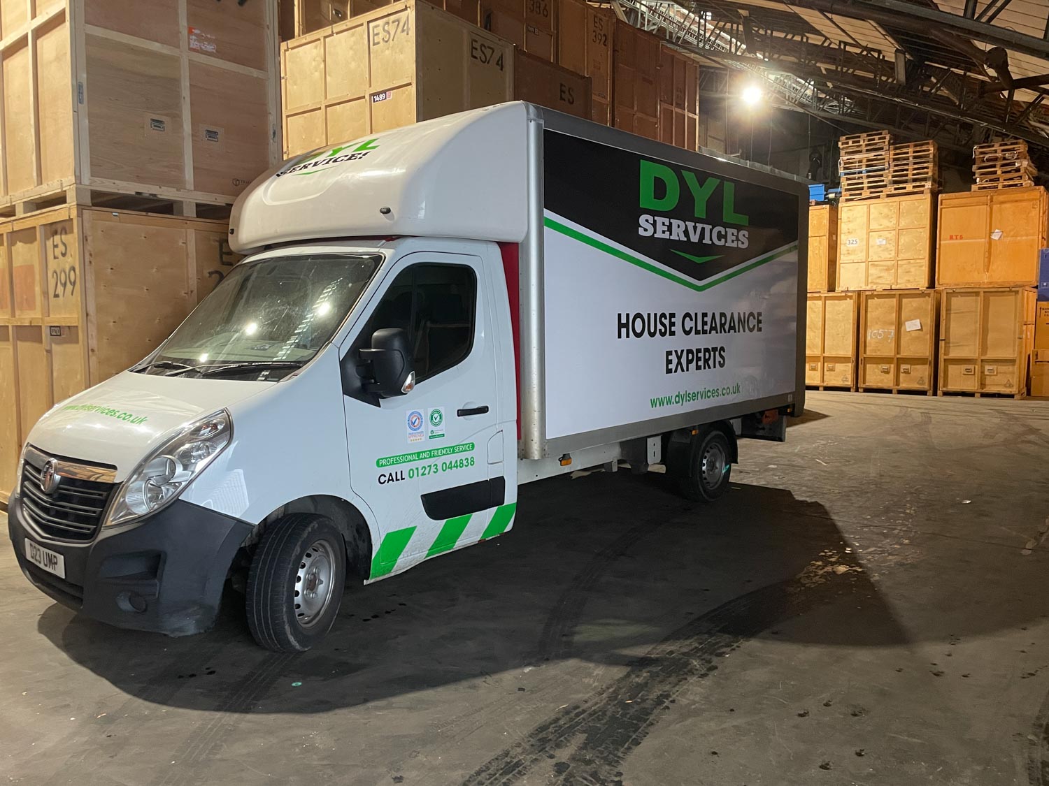 A delivery truck labeled "DYL Services" is parked inside a warehouse with wooden crates.