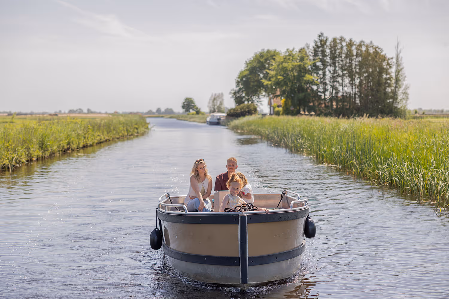Gezin met twee volwassenen en twee kinderen geniet van een boottocht met een e-sloep op een smal kanaal in het groen.