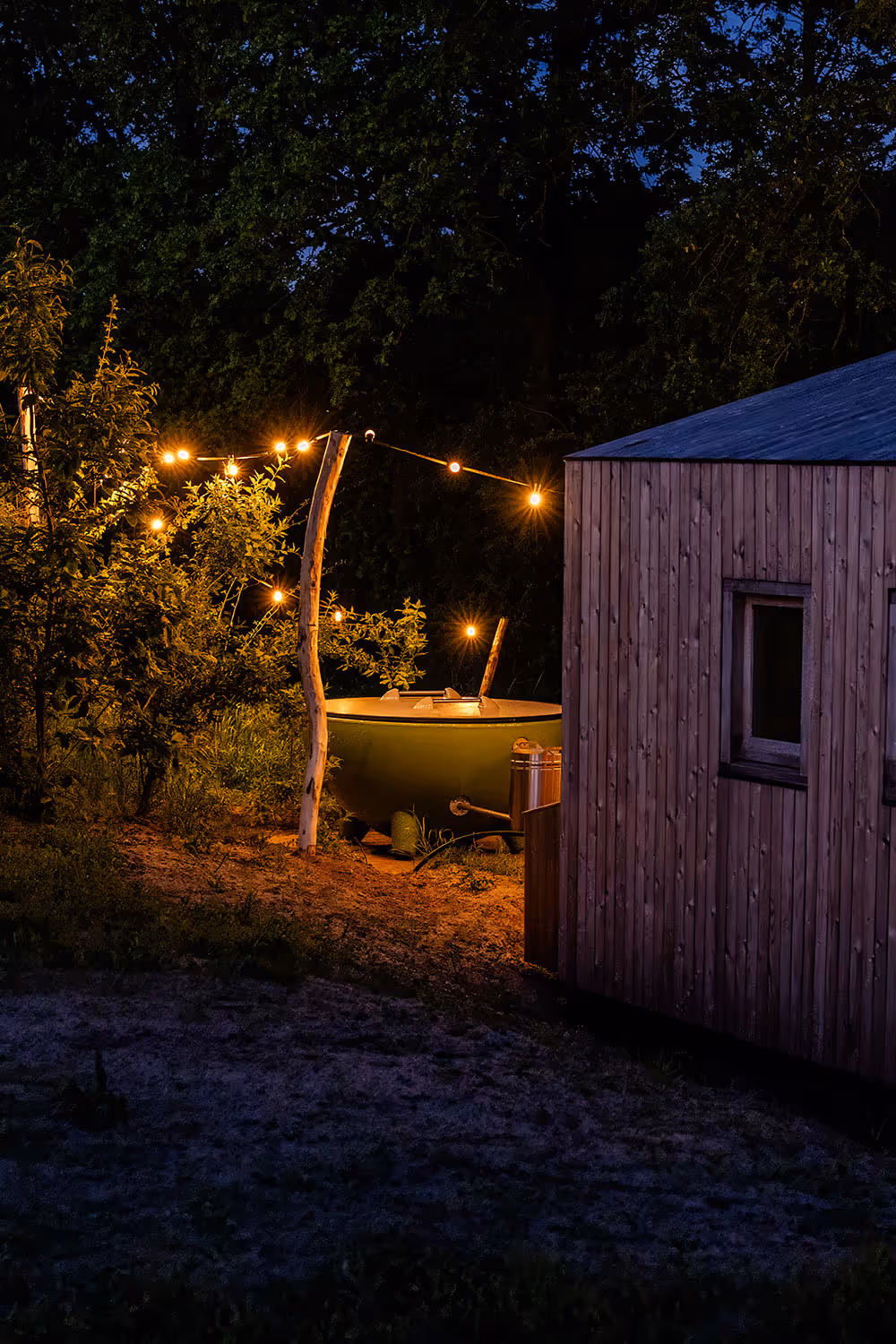Nachtzicht op een hout gestookte hottub van Weltevree naast een vakantiehuisje in Friesland met sfeerverlichting buiten.