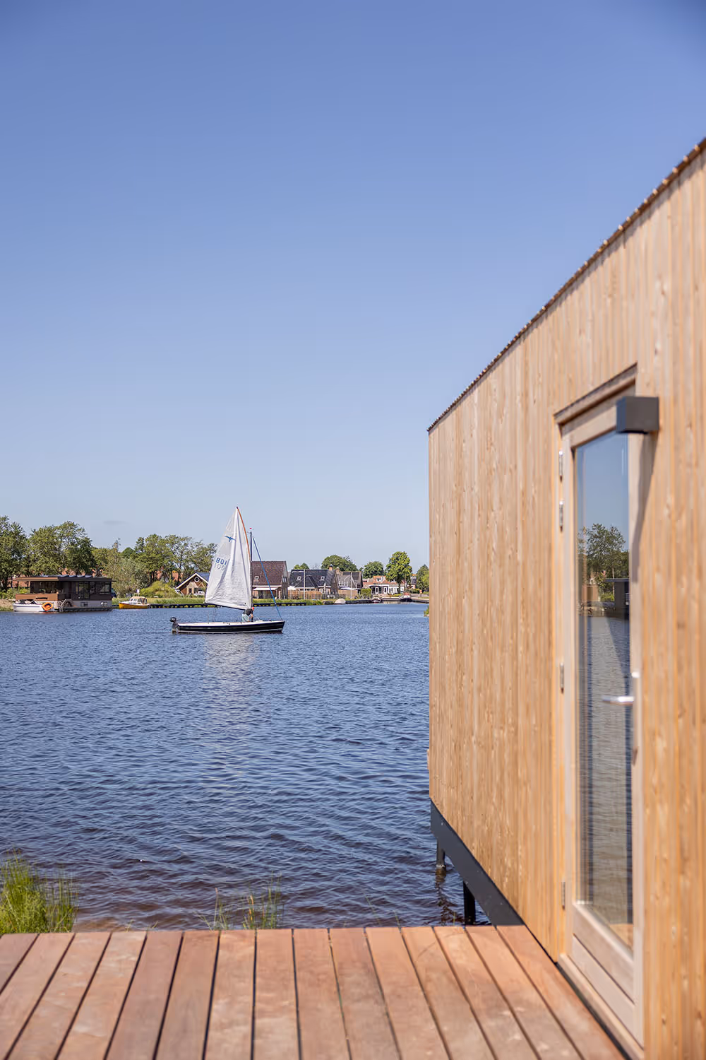 Waterlodge in Friesland aan het water met een zeilboot op een rustige rivier bij helder weer.