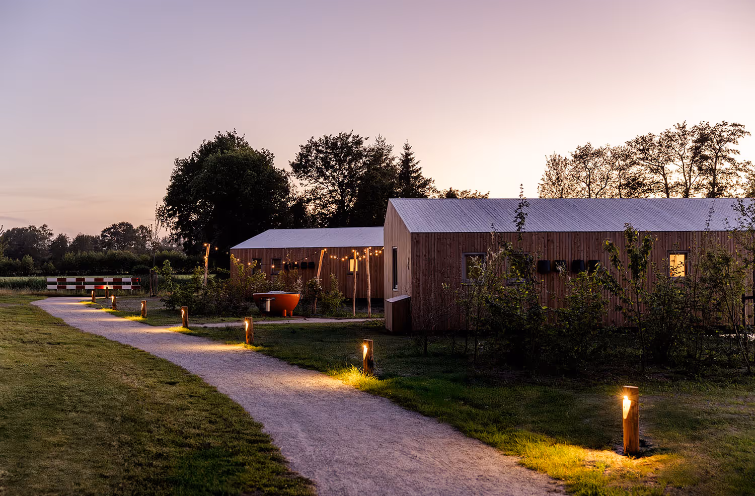 Verlicht wandelpad langs bijzondere oeverlodges en waterlodges met hot tub in natuur tijdens schemering.