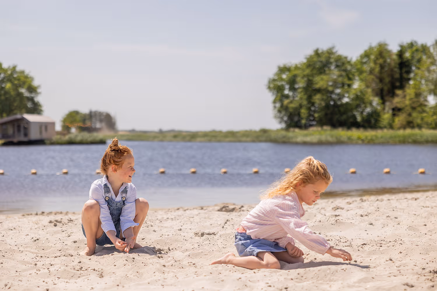 Twee meisjes spelen in het zand aan de oever van van Goudpoel in Friesland. Ze zijn op vakantie.