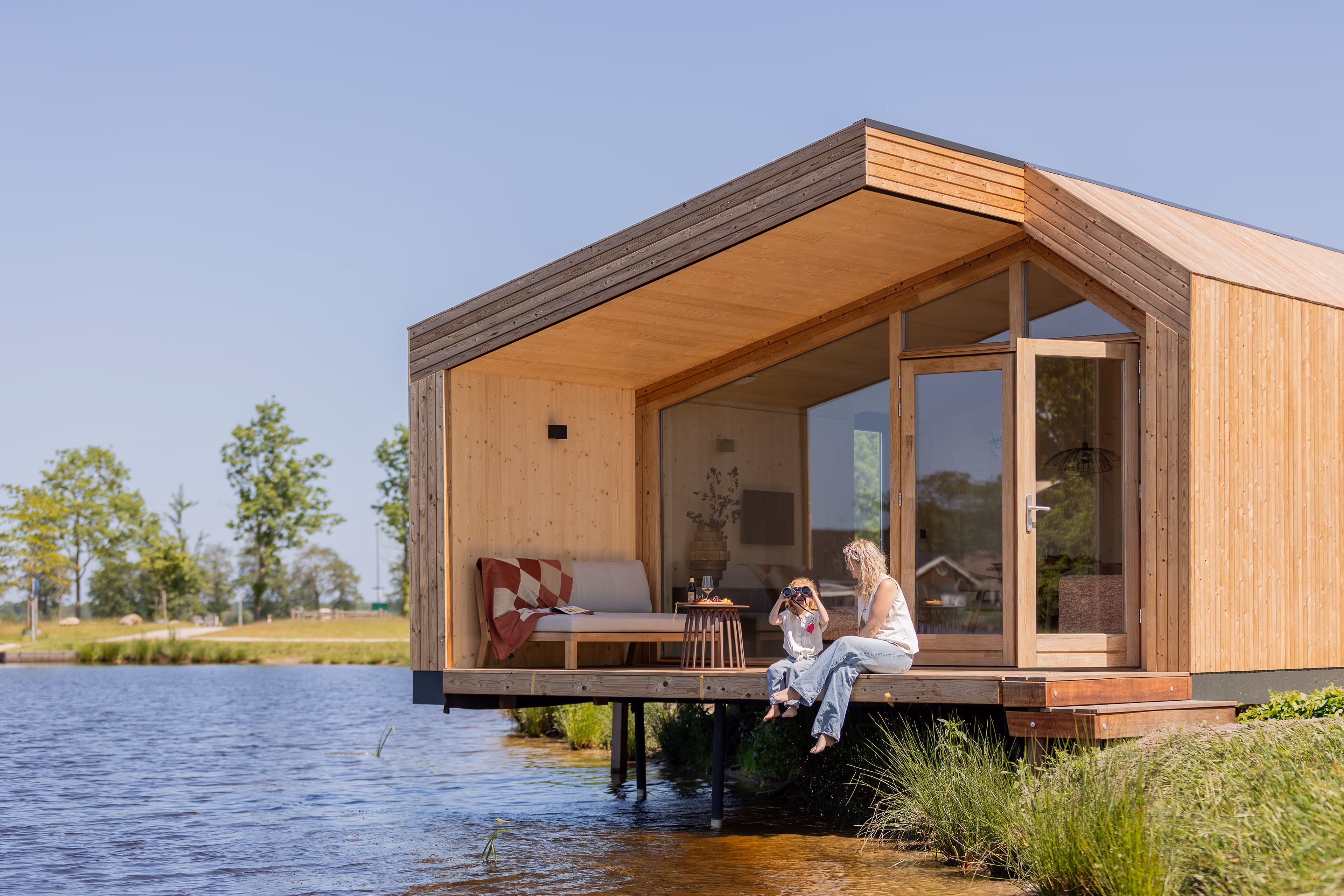 Moeder en kind zitten op veranda van een vakantiehuisje in Goudpoel Friesland. Kind kijkt door verrekijker.