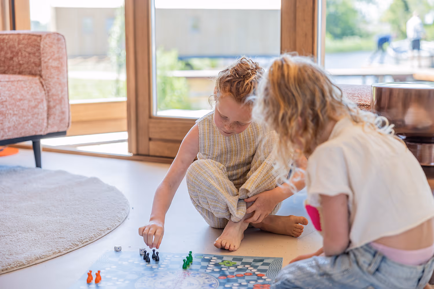 Twee kinderen zitten op de grond en spelen een bordspel in een lichte woonkamer met grote ramen. Het is op vakantiepark Goudpoel in Oudga in Friesland.
